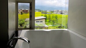 Un baño con bañera, ventana y vista a una zona residencial con casas y zonas verdes.