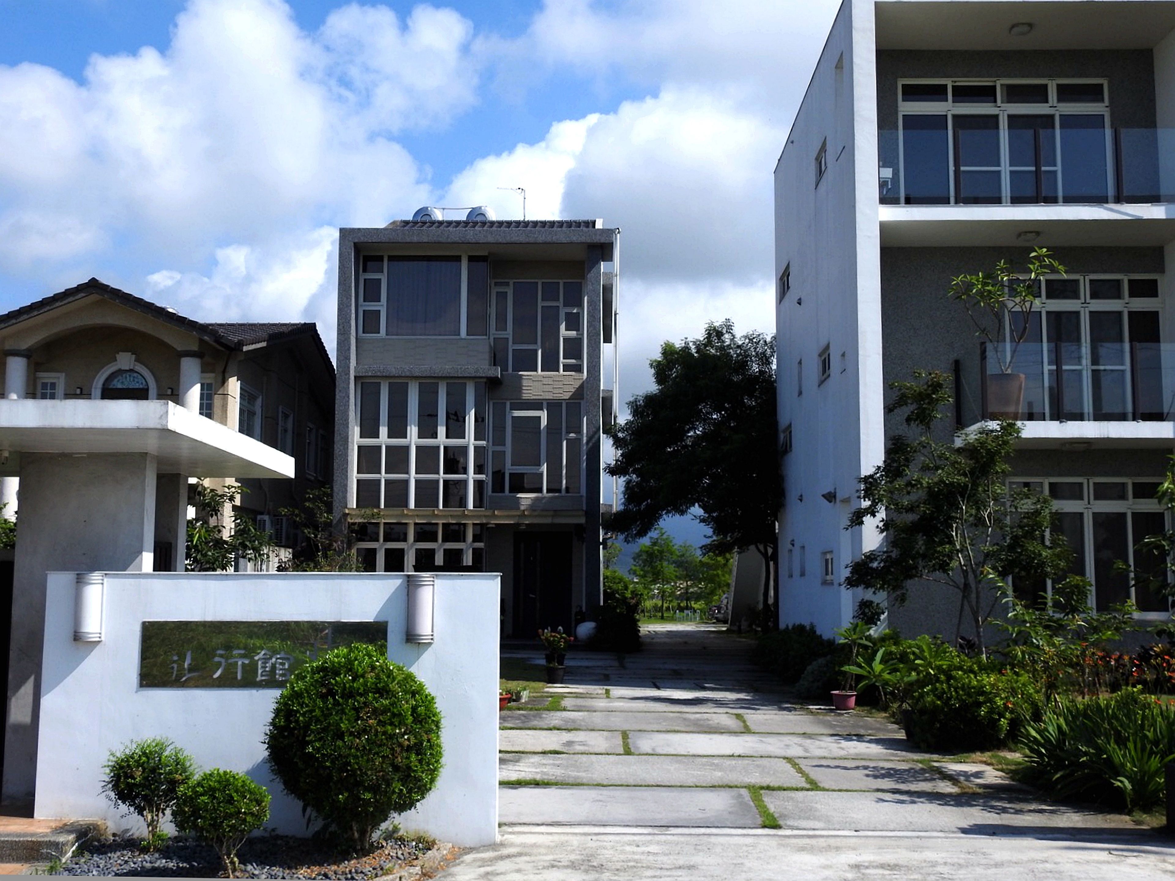 Un edificio moderno con una entrada central, rodeado de vegetación y un cielo despejado.