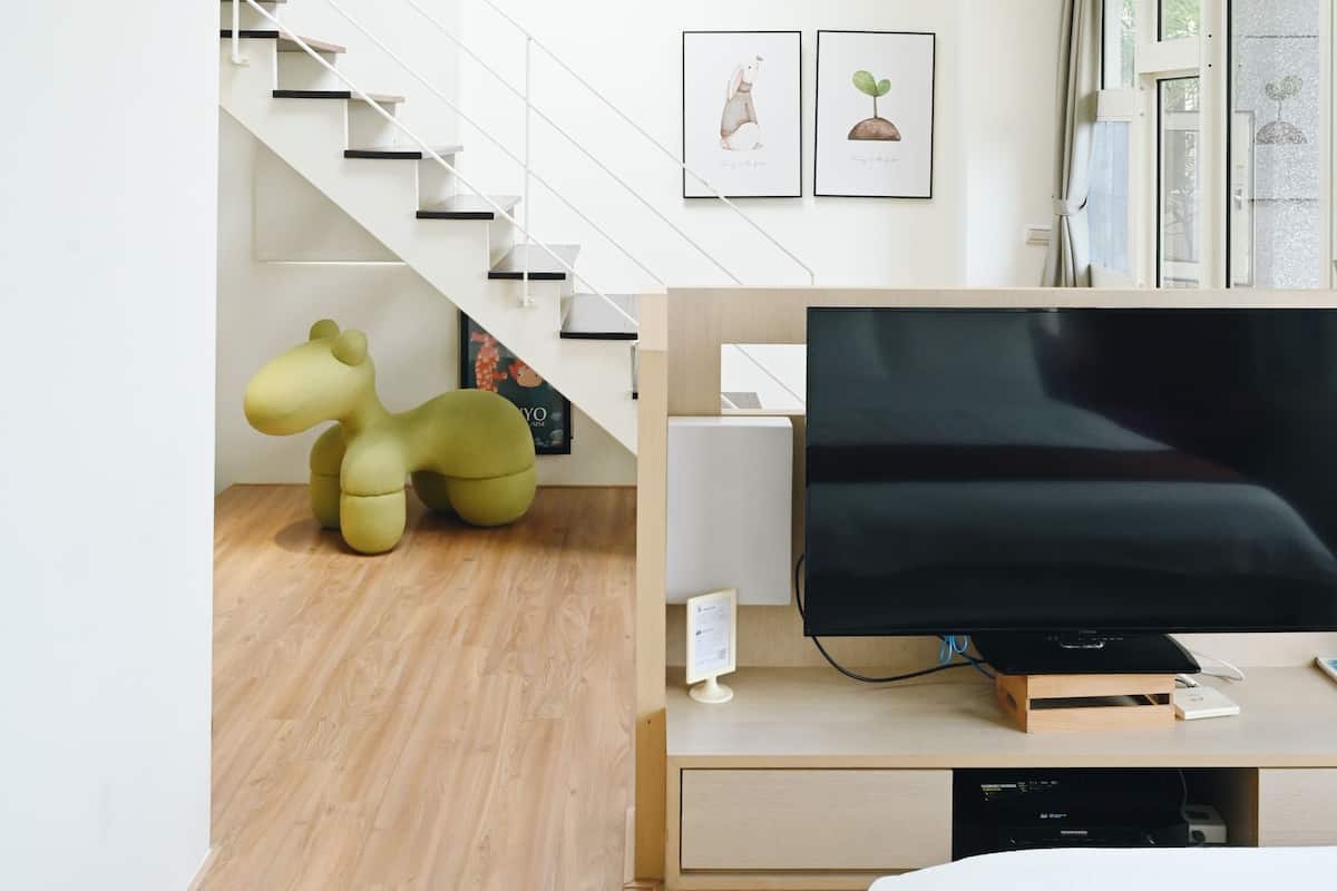 A modern living room with a flat-screen TV, a staircase, and a large window.
