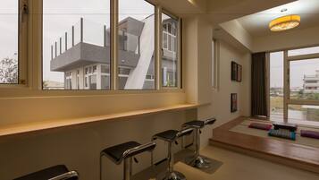 A modern interior with large windows, a wooden bench, and a bar area with stools.