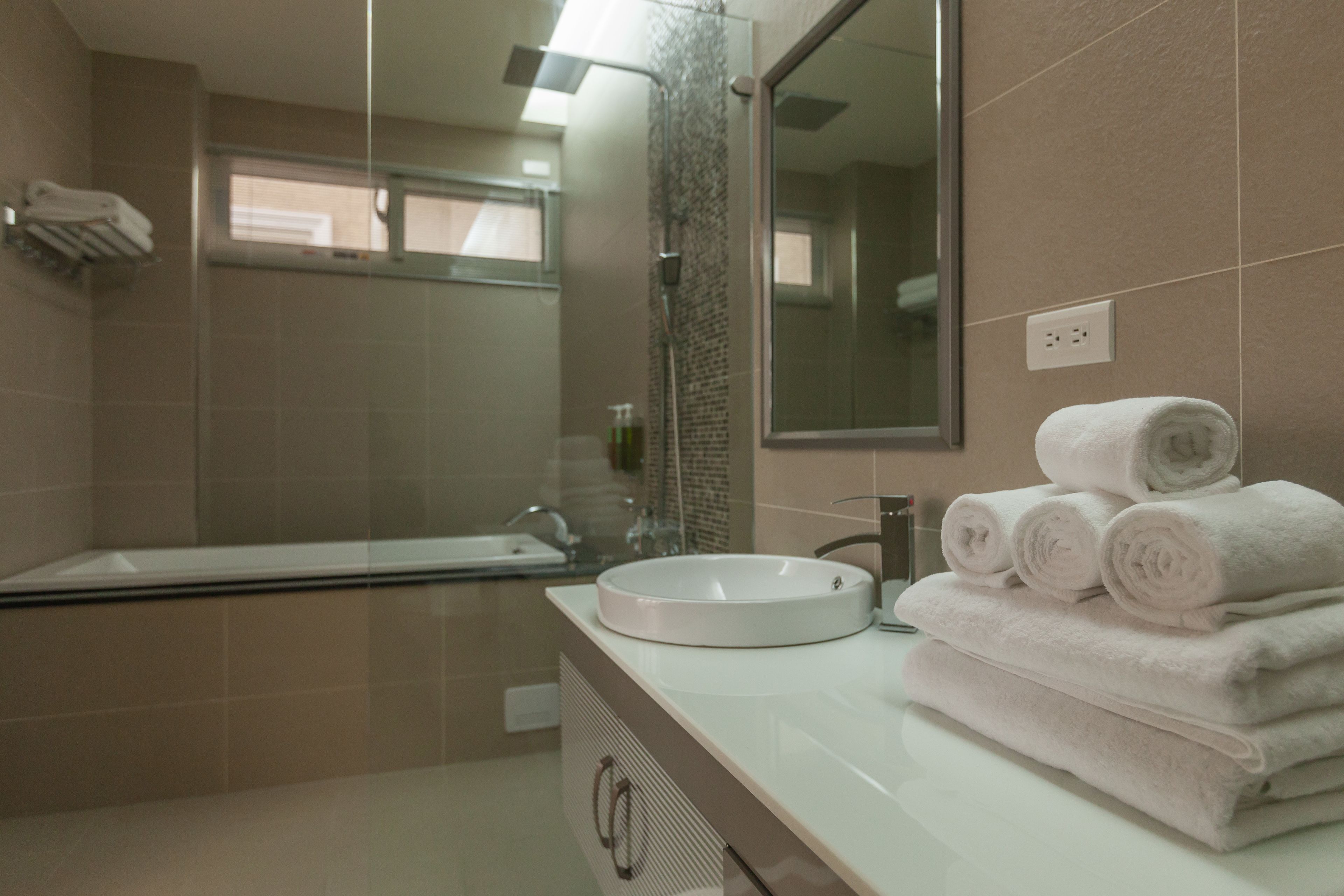 A modern bathroom with a bathtub, a round sink, and a stack of towels.