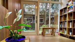 Una habitación con piso de madera, un tapete azul, un banco de madera, una estantería y una planta en maceta.