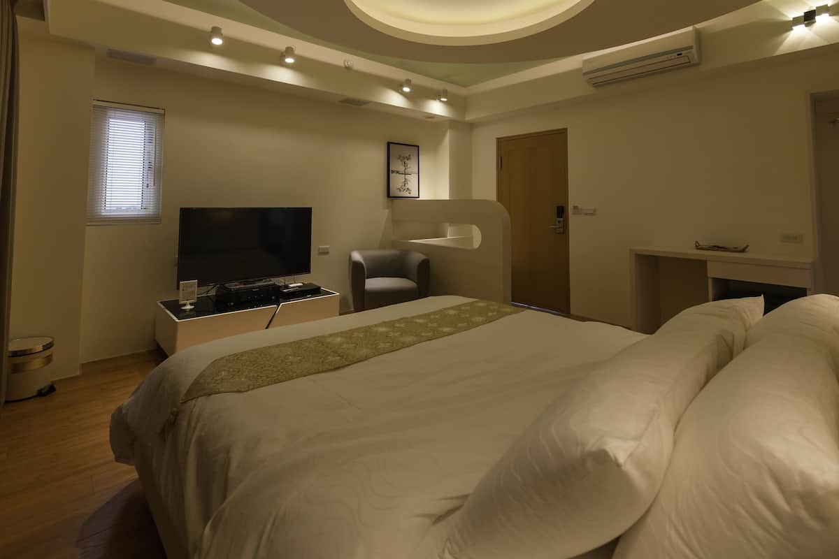 A modern hotel room with a large bed, a flat-screen TV, a desk with a computer, and a small seating area.
