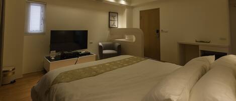 A modern hotel room with a large bed, a flat-screen TV, a desk with a computer, and a small seating area.