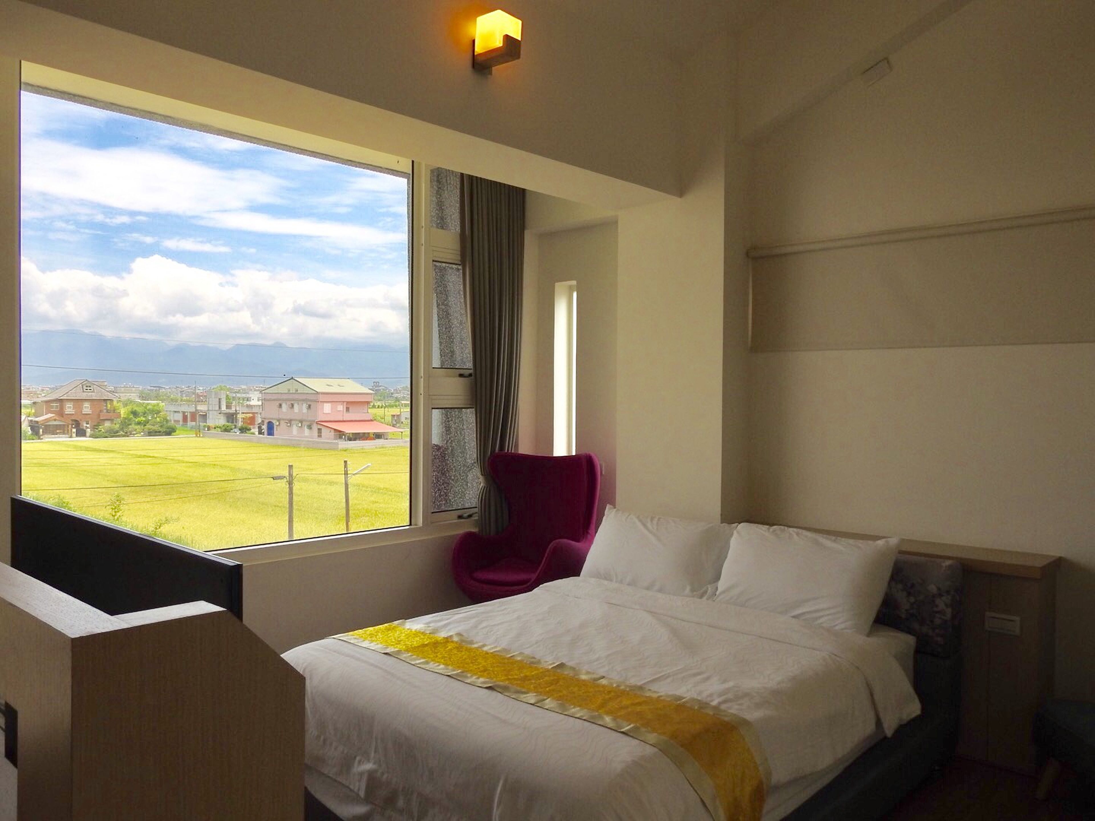 Une chambre d’hôtel dotée d’une grande fenêtre donnant sur un champ verdoyant et des bâtiments.