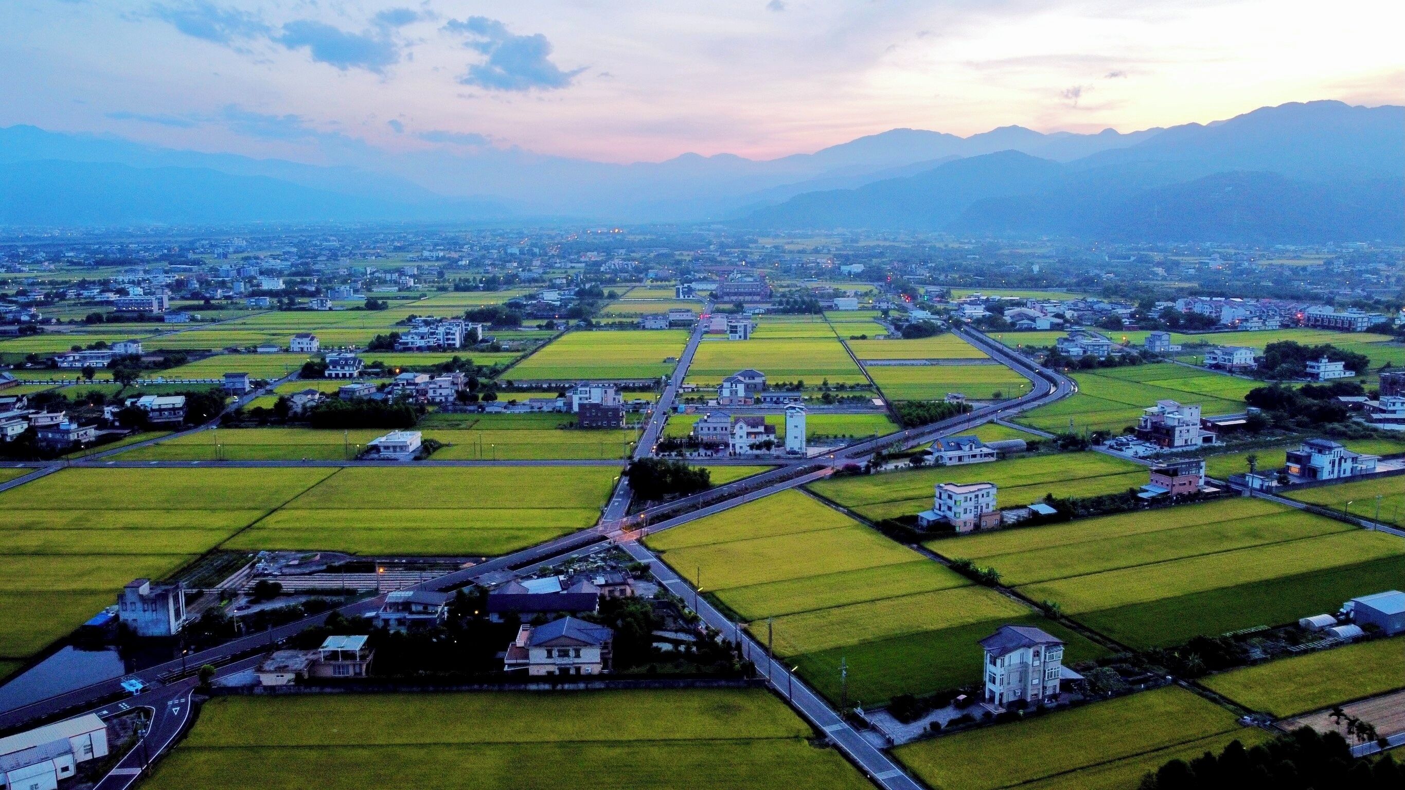 An aerial view of a town with green fields, roads, and buildings.