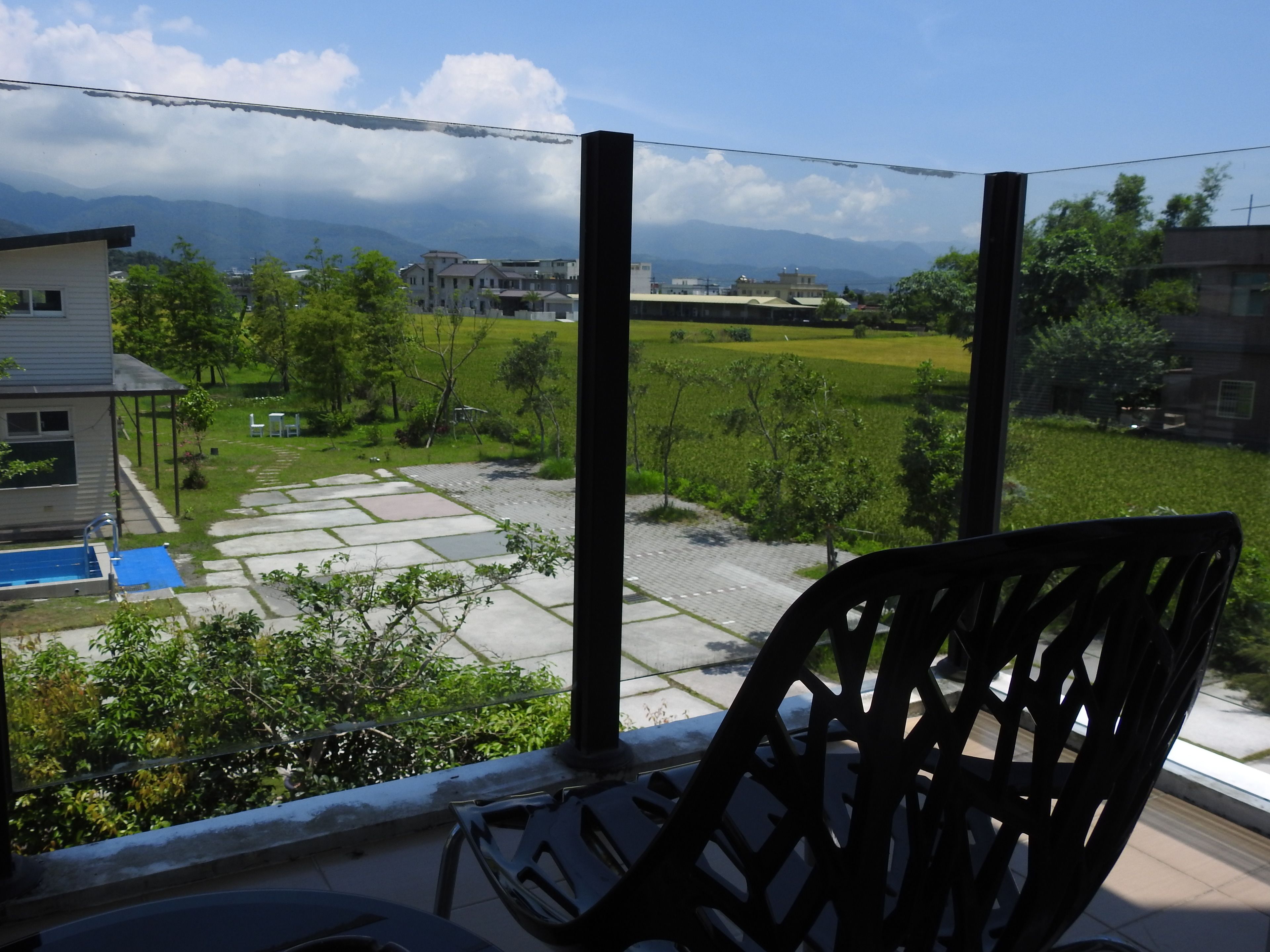A balcony with a view of a residential area, including houses, a swimming pool, and a paved path.