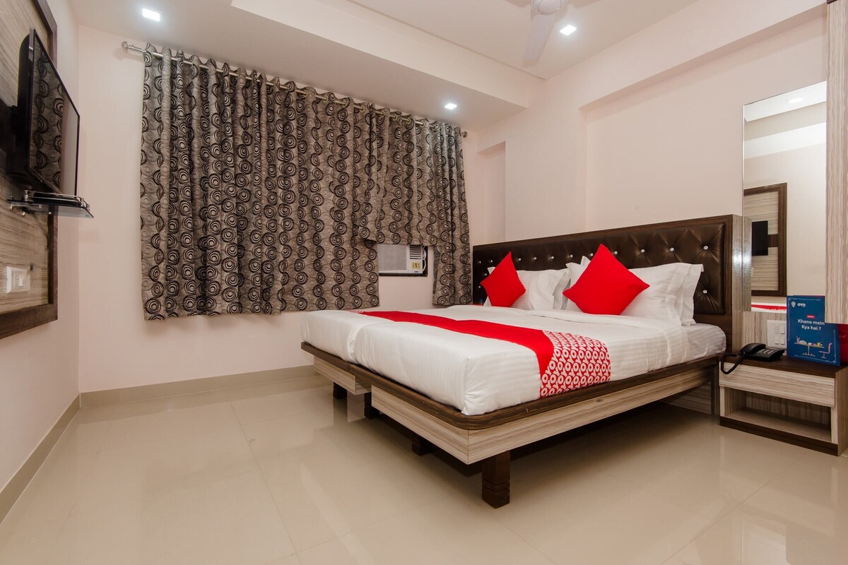A hotel room with a large bed, a TV, a bedside table, and a mirror.