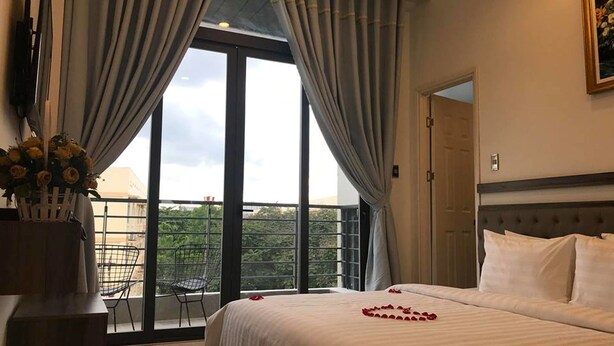 Habitación de hotel con una cama grande, un balcón con una silla y vistas a zonas verdes.
