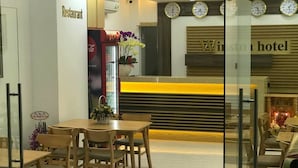 Vestíbulo de hotel con mostrador de recepción, un reloj y el letrero de un restaurante.