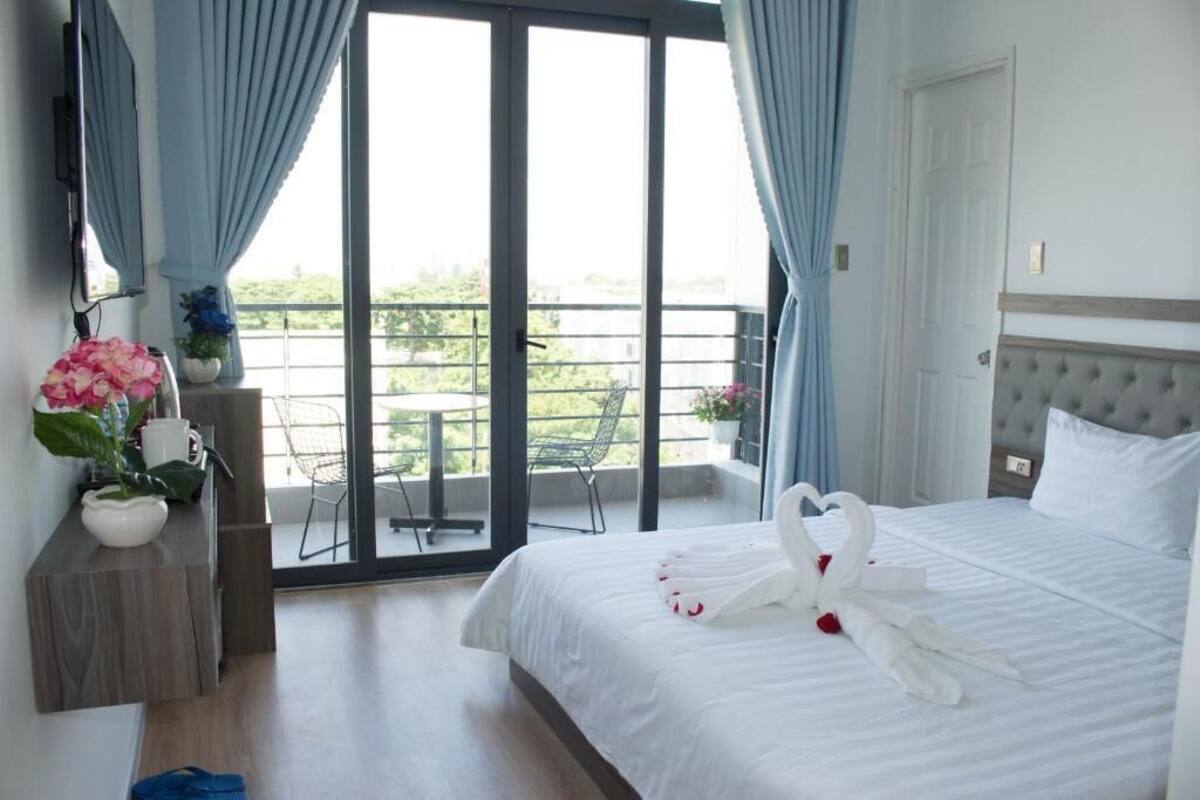 A hotel room with a bed, a balcony with a chair, and a view of greenery.
