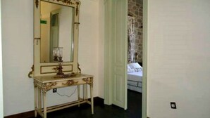 A room with a large ornate mirror on a console table, a bed with white bedding, and a stone wall in the background. - Cunda Has Konak Otel (Ayvalik)