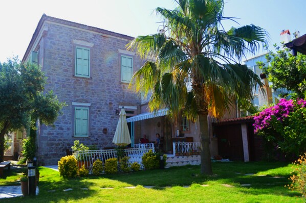 A stone building with a balcony, a palm tree, and a garden with flowers.