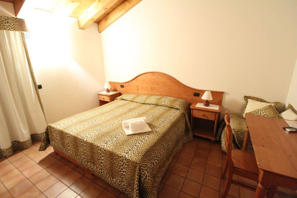 A bedroom with a bed, wooden headboard, bedside tables, a wooden chair, and a table.