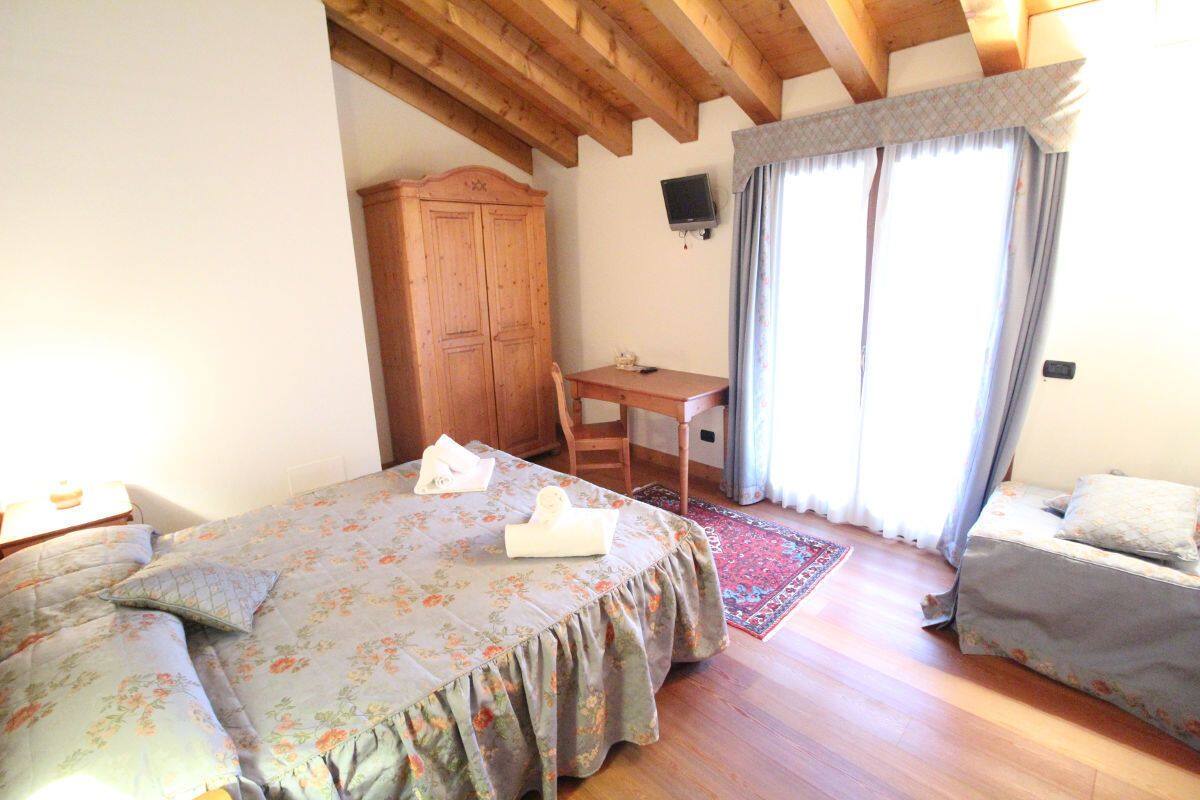 A bedroom with a bed, a desk, a chair, a wardrobe, and a television.