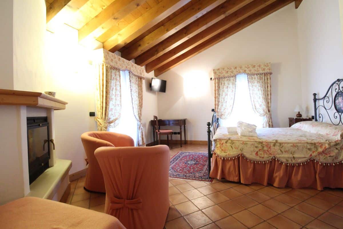 A bedroom with a bed, a television, a fireplace, and a window with curtains.