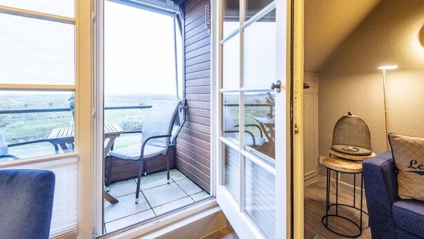 Una habitación con puerta corrediza de vidrio que da a un balcón con una silla y una mesa.