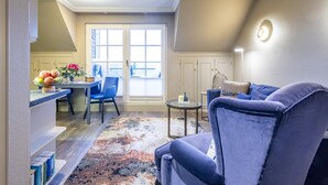Una sala de estar con un sillón azul, un comedor con mesa y sillas, y vistas al exterior a través de un ventanal.