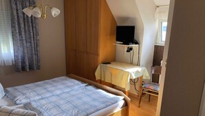 A bedroom with a bed, a desk with a TV, and a chair. - Hotel Kreta (Ueberlingen)