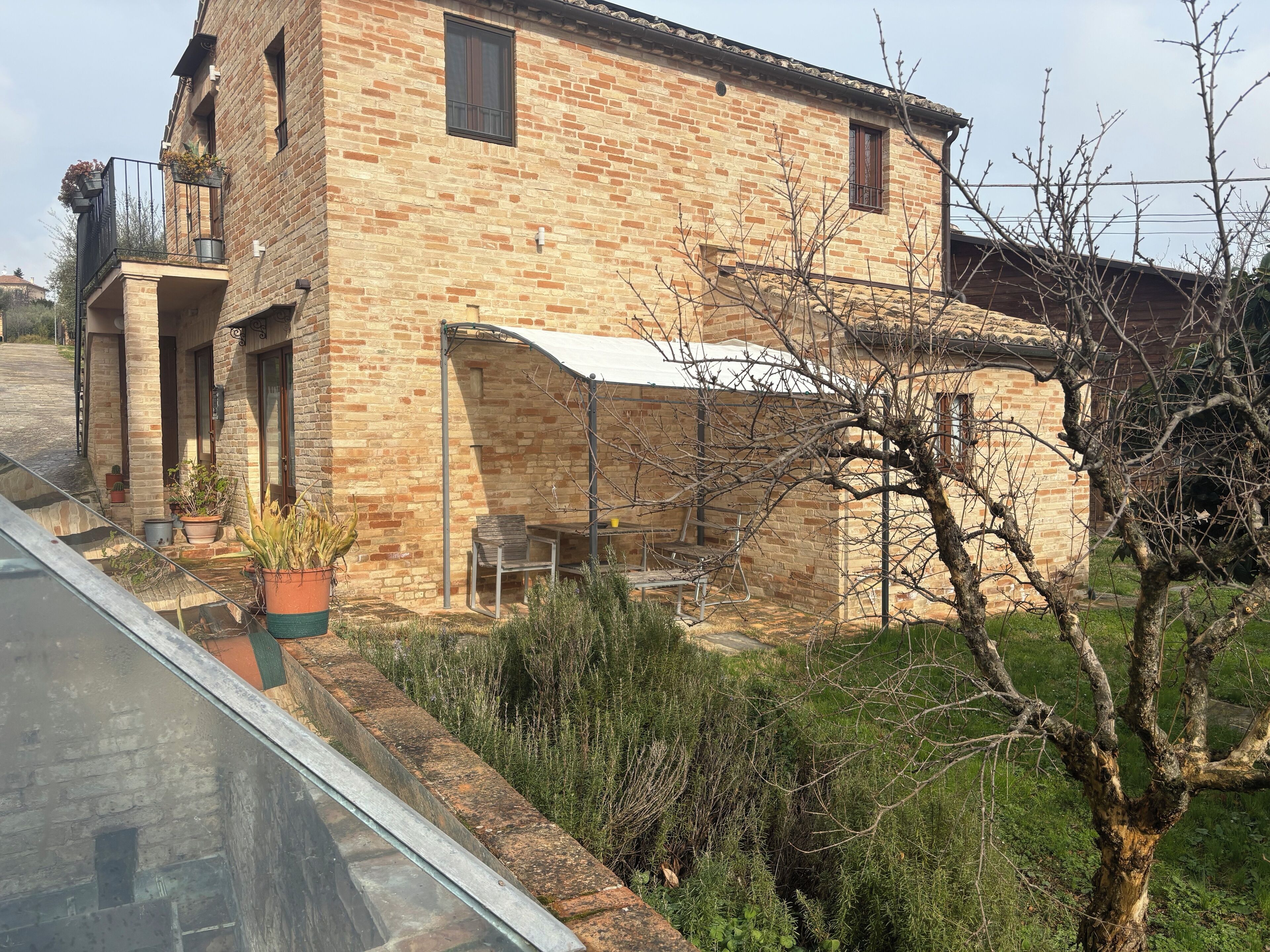 A rustic brick house with a balcony, a small table, and potted plants.
