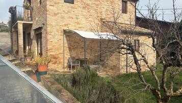A rustic brick house with a balcony, a small table, and potted plants.