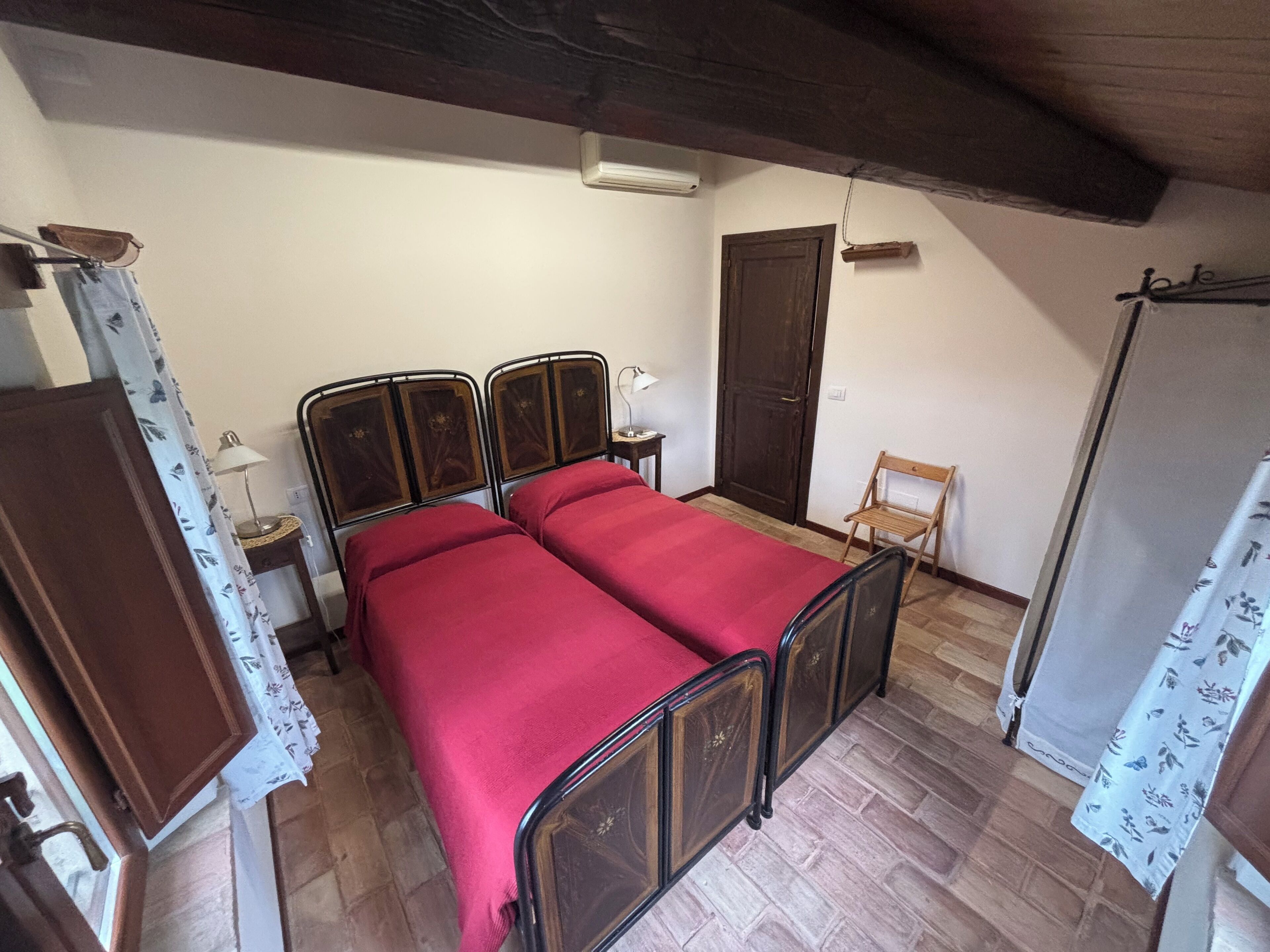 A bedroom with a double bed, a wooden door, a small table with a lamp, and a chair.