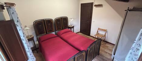 A bedroom with a double bed, a wooden door, a small table with a lamp, and a chair.
