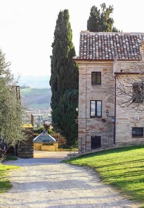 Un edificio de piedra con tejado de tejas, camino de grava y vistas al campo.