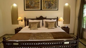 Una cama tamaño king con estructura de madera, dos lámparas fijadas a la pared y dos cuadros con estampados de tigres encima.