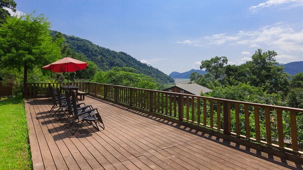A wooden deck with outdoor furniture and a red umbrella, overlooking a lush green landscape and a valley. - Locasu B&B (Datong)
