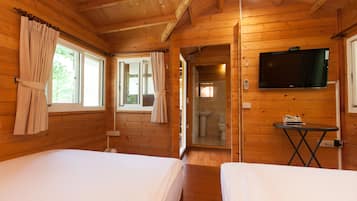 Habitación de cabaña de madera con dos camas, un televisor y un baño visible a través de una puerta abierta.