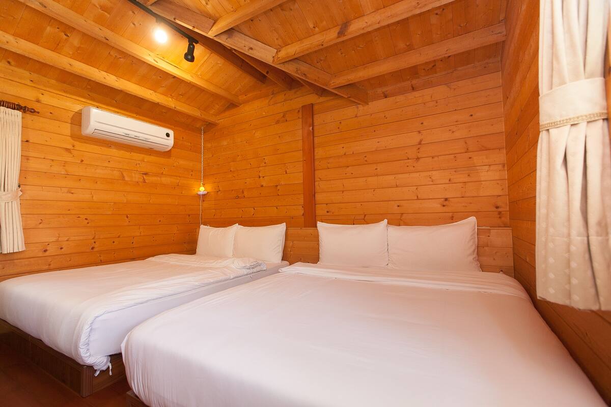 A wooden cabin room with two beds, an air conditioning unit, and a hanging light fixture.