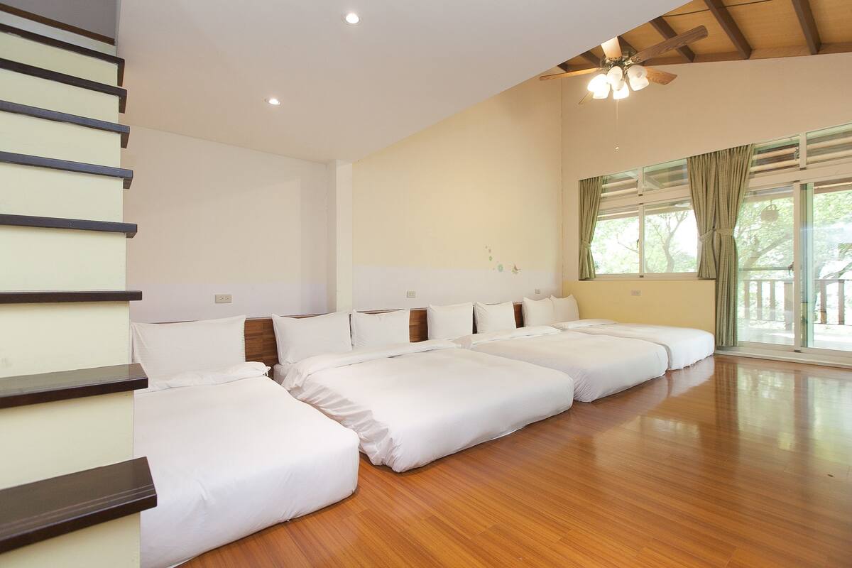 A large room with three beds aligned against a wall, wooden flooring, and a ceiling fan.