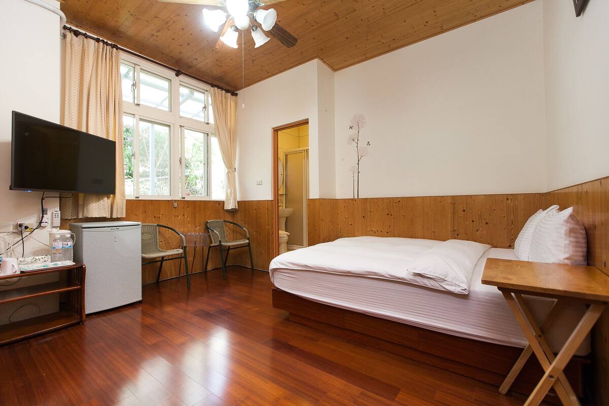 A room with a bed, a television, a small refrigerator, and a window with curtains.
