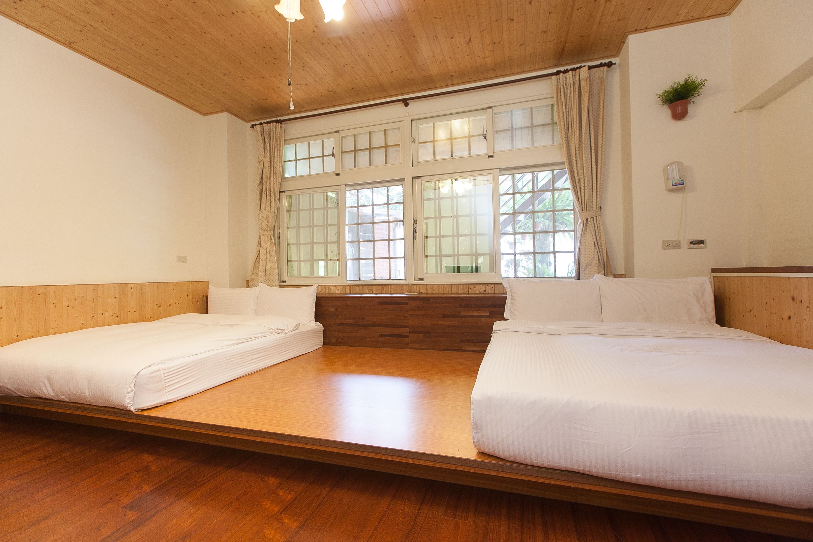 Una habitación con dos camas individuales, suelo de madera, un ventanal grande con cortinas y techo de madera.