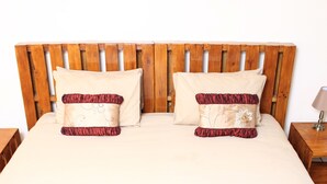 A bed with a wooden headboard, two pillows with a red and beige design, and a bedside table with a lamp. - Unique Bed and breakfast (Harare)