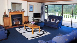 A living room with a fireplace, a television, a sofa, and a large window with a view of greenery. - Unique Bed and breakfast (Harare)