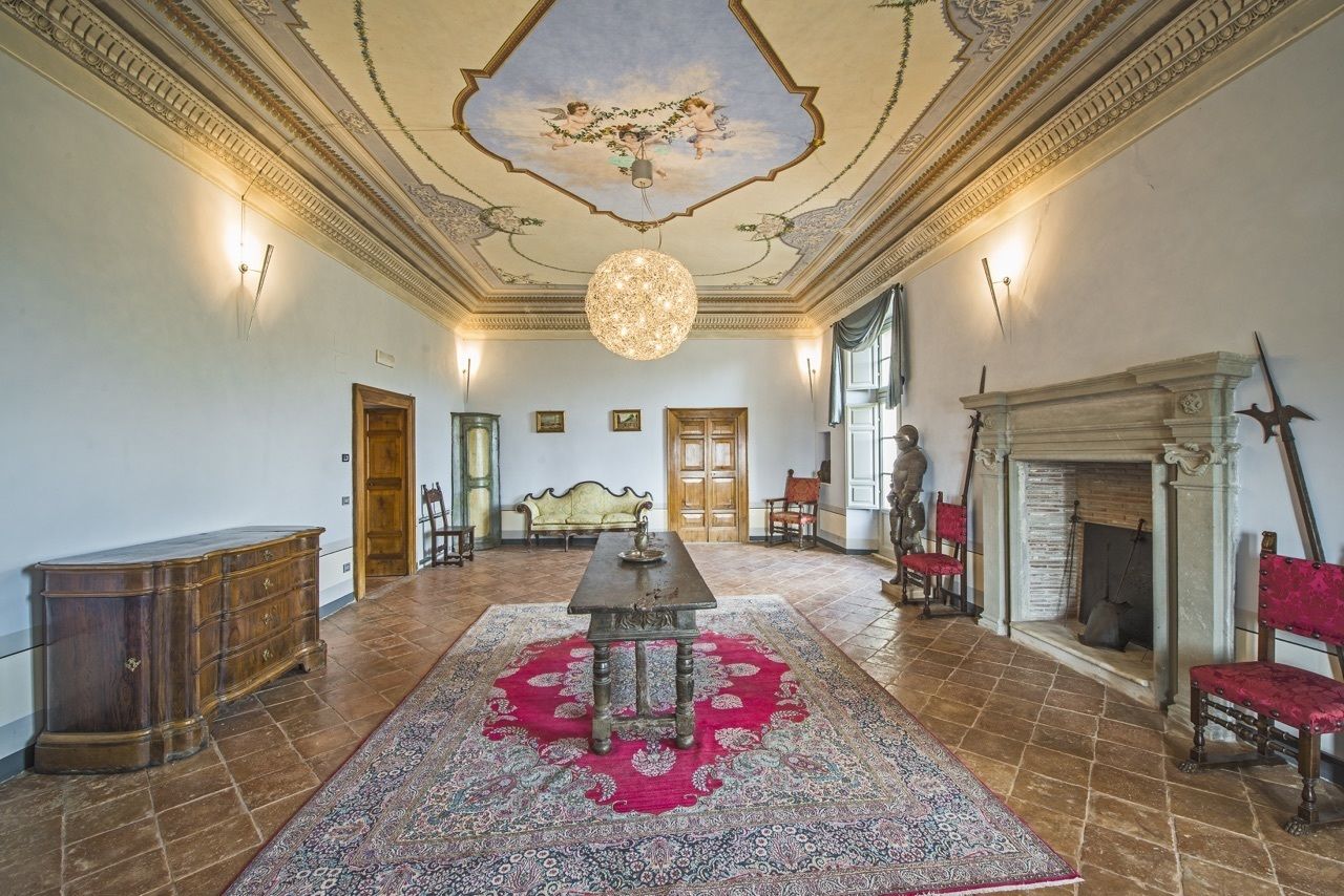 A spacious room with a large ornate chandelier, a fireplace, and a red patterned rug.