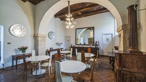 Un comedor con mesas y sillas redondas, techo de madera y pared de piedra.