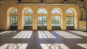 Un amplio salón con grandes ventanales de arco, techo alto con vigas a la vista y un candelabro central.