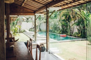 Comedor de madera con vista a una piscina y exuberante vegetación.