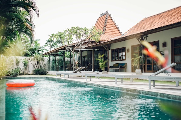 A swimming pool with a clear water surface, a red inflatable float, and a building with a tiled roof and large windows.