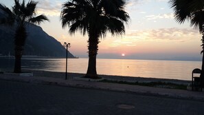Sonnenuntergang über einem ruhigen Meer mit Palmen und einem Berg im Hintergrund.