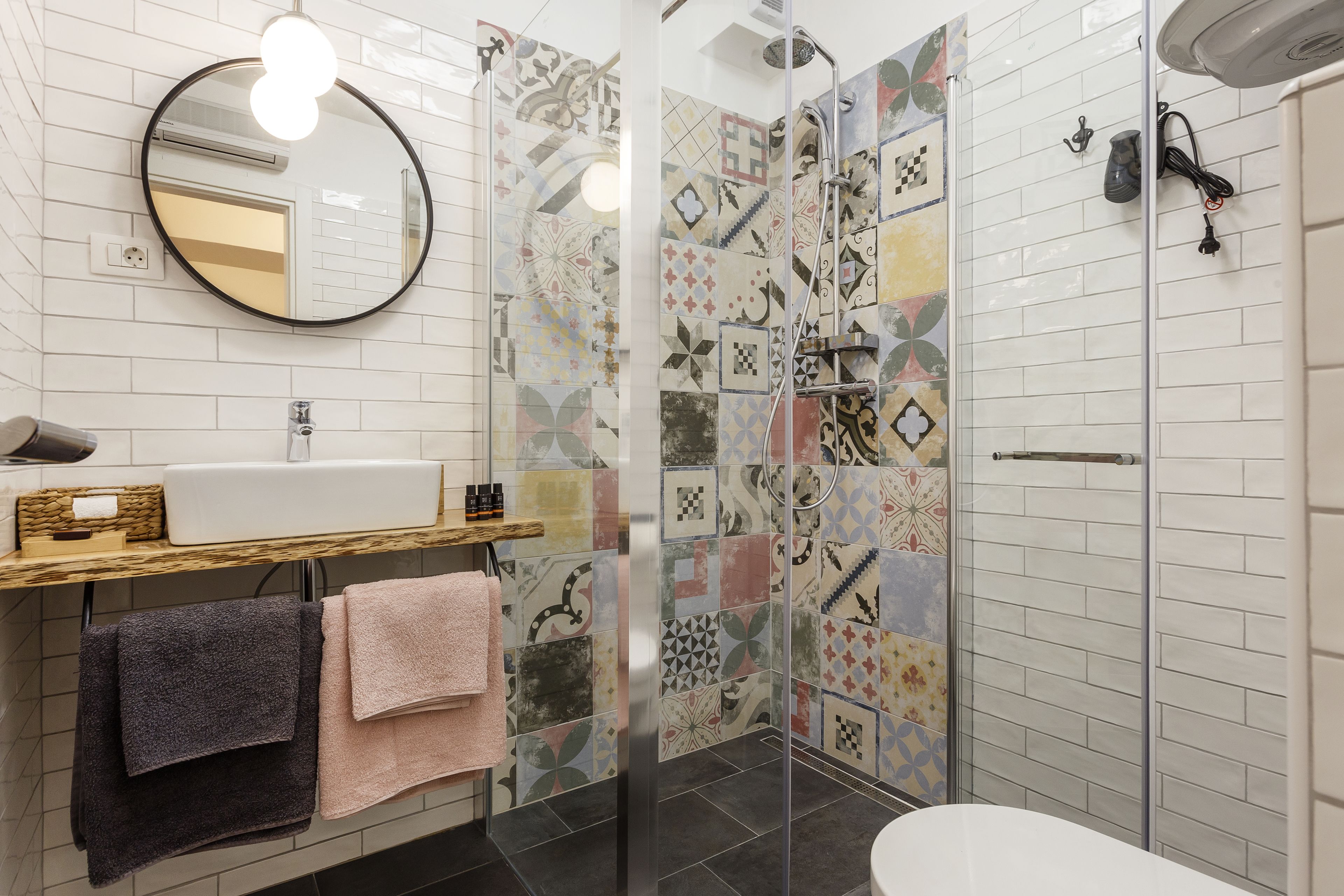 A bathroom with a white sink, mirror, and tiled walls. There is a shower area with a glass door and a toilet.
