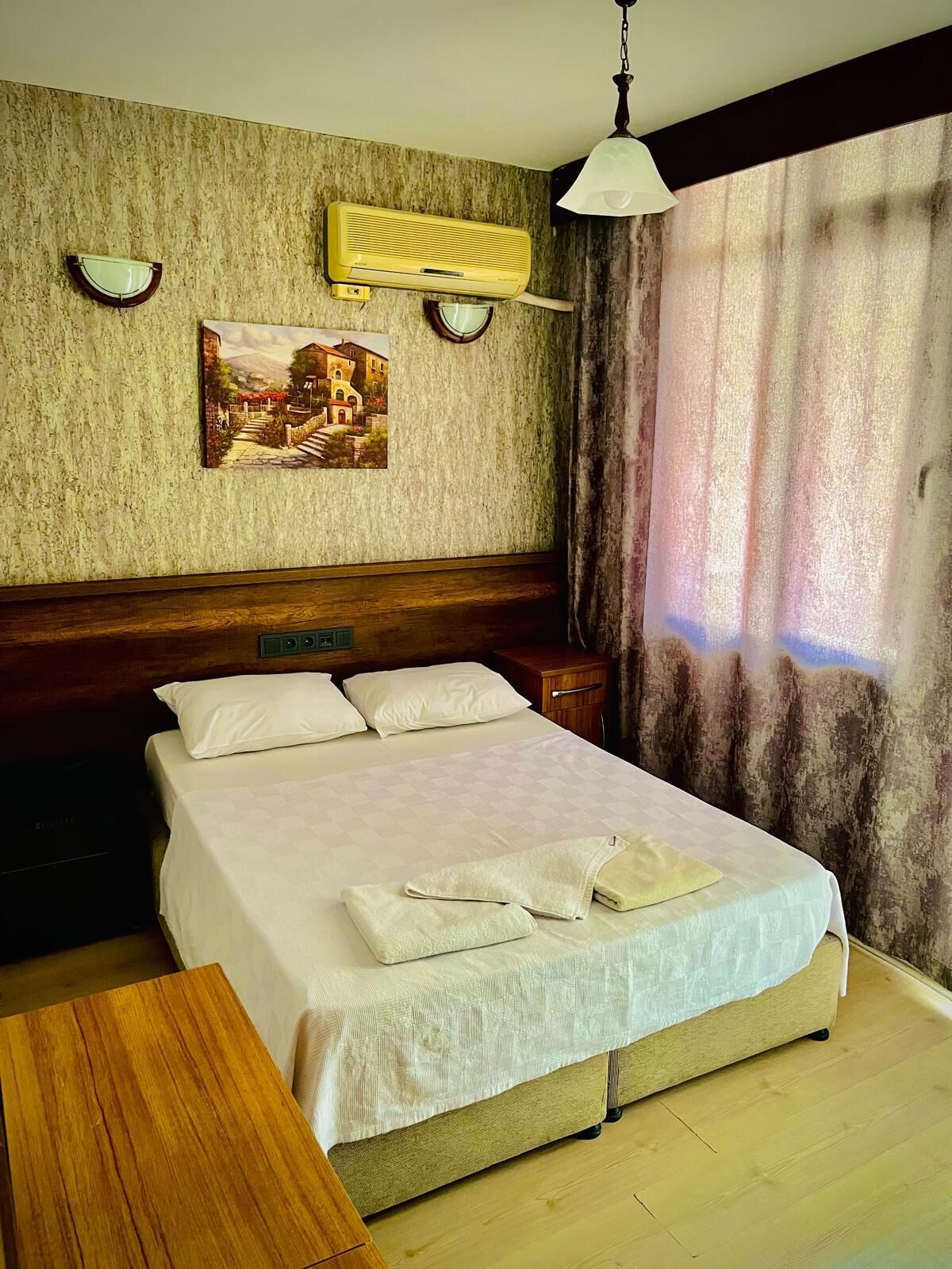 A hotel room with a bed, bedside table, and a painting on the wall.