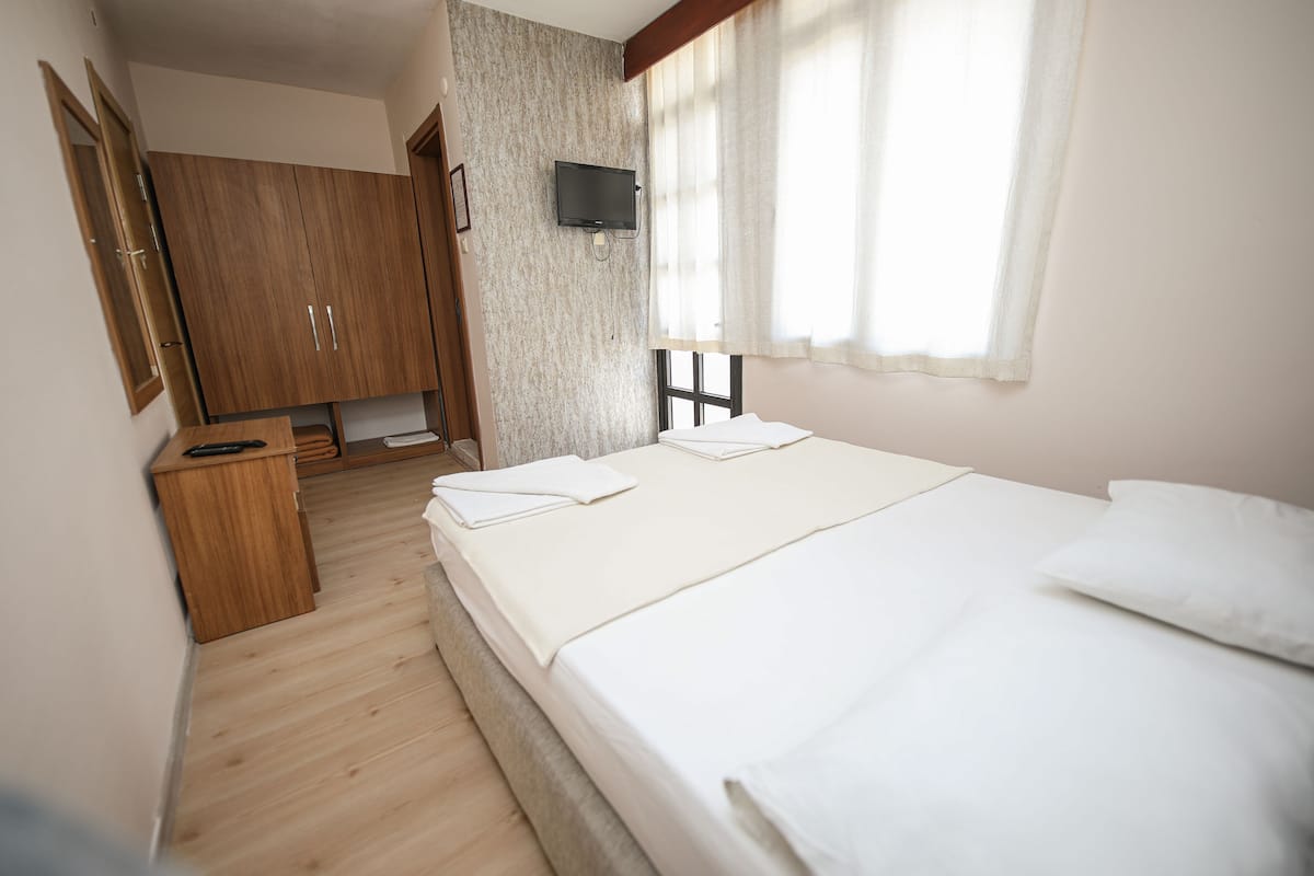 A bedroom with a bed, wooden wardrobe, and a TV mounted on the wall.