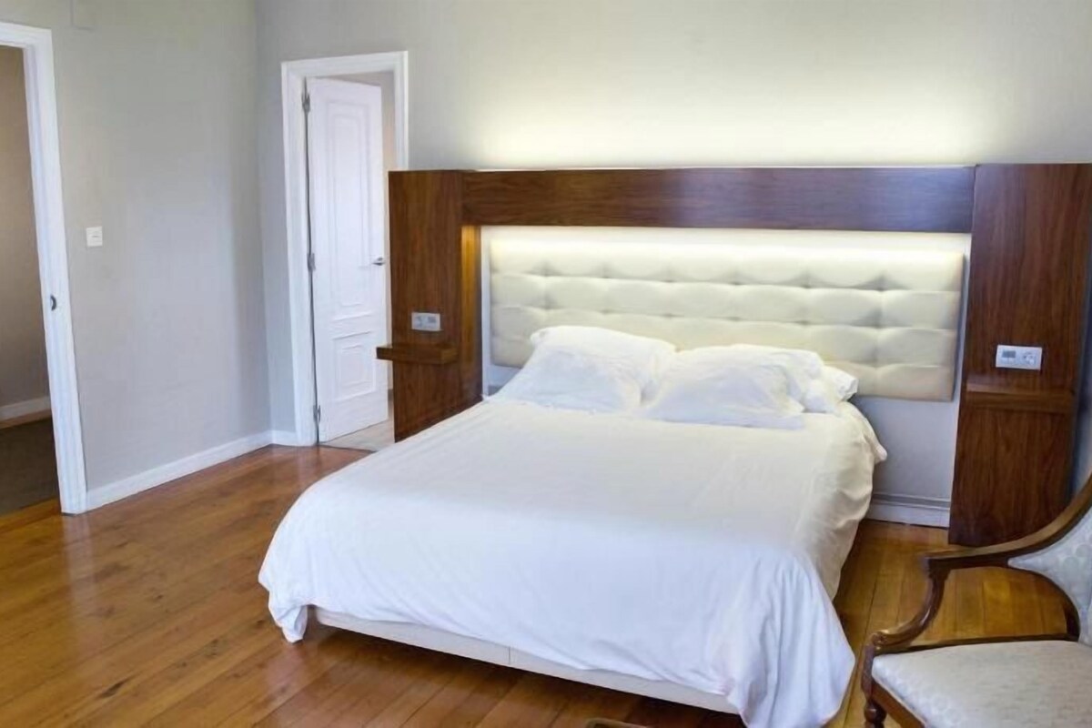A bedroom with a large bed, wooden floor, and a chair.
