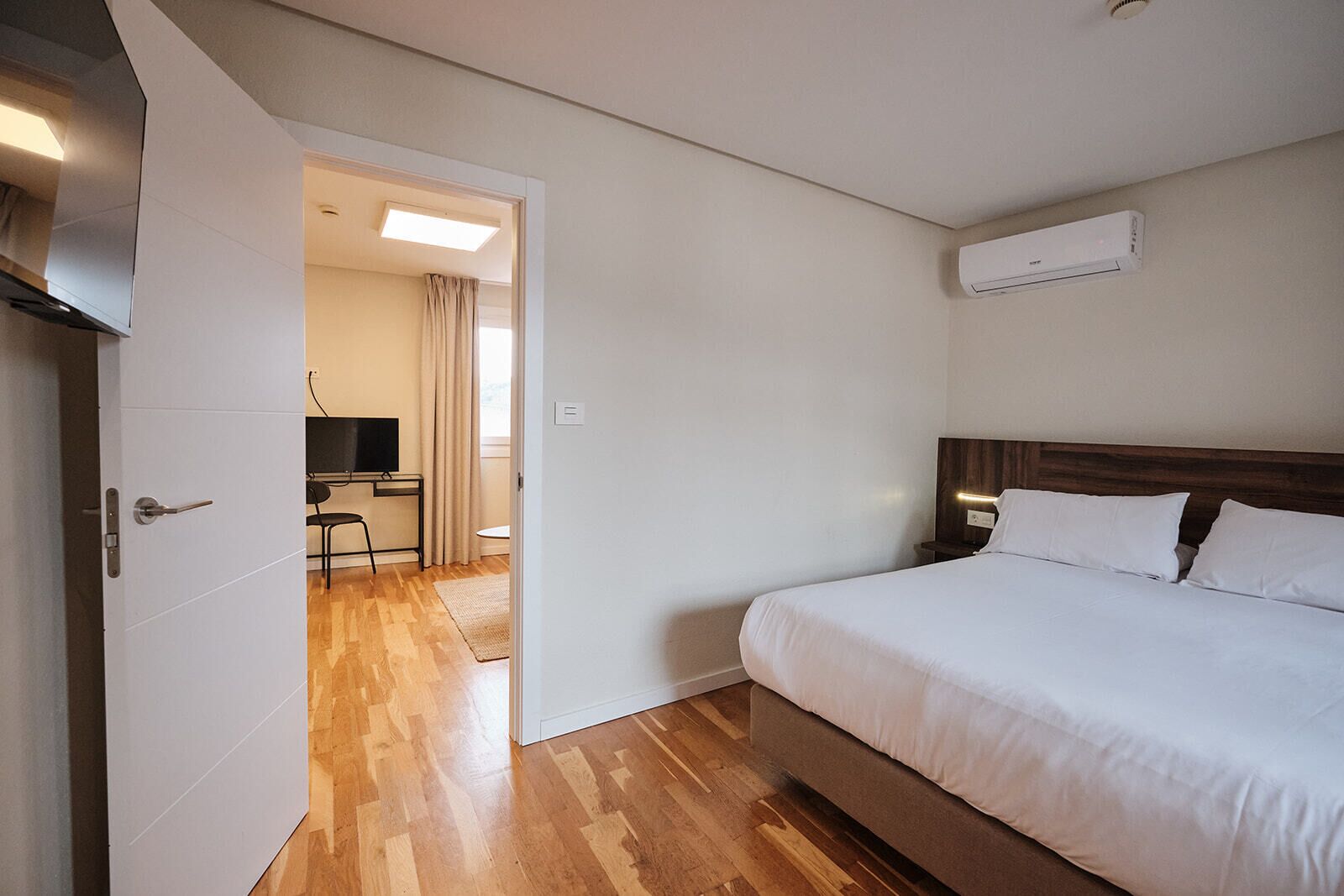Habitación de hotel con cama, escritorio, silla, televisor y aire acondicionado.