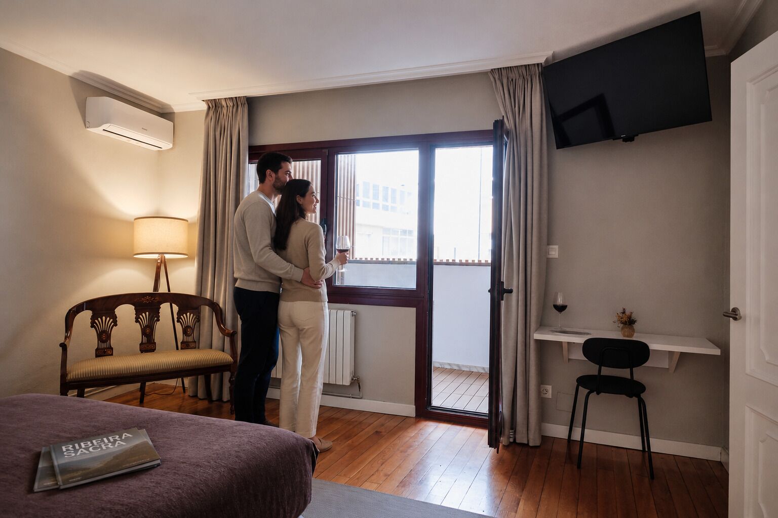 A hotel room with a bed, a desk, a chair, a TV, and a window with curtains.