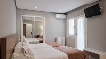 Un dormitorio con cama, espejo, televisor y ventana.